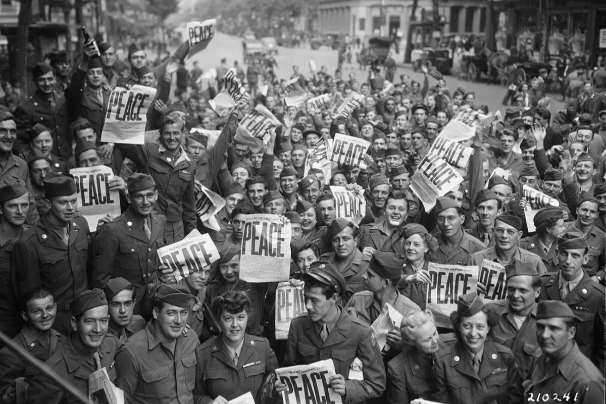 Esta fotografía capta a un grupo multitudinario de soldados y personal militar estadounidense celebrando el fin de la Segunda Guerra Mundial en Europa y el Pacífico. La imagen fue tomada en la famosa esquina conocida como Rainbow Corner del club de la Cruz Roja Americana en París, Francia. Fuente: National Park Service